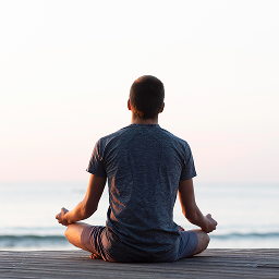 Man meditating on wooden pier at sunset