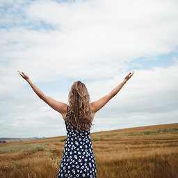 Woman standing in field with open arms under blue sky